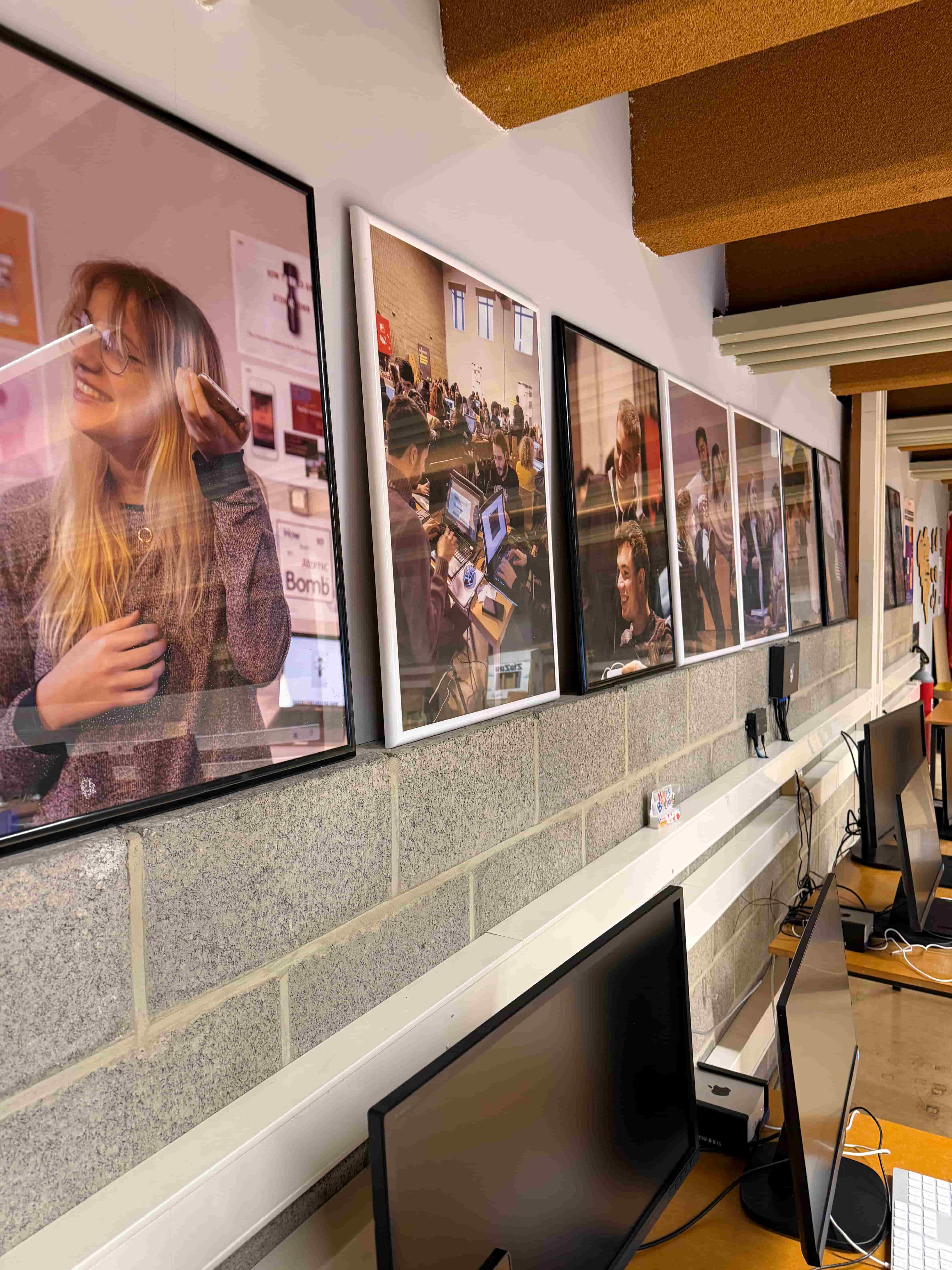 photo prise de coté où l'on voit une rangée de cadre sur un mur avec des photos de personnes qui travaillent
